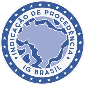 Imagem colorida que mostra o selo de Indicação de procedência IG Brasil. Este selo é circular e possui dois anéis e um círculo. O anel mais externo de cor azul, com várias estrelas de cor branca dentro. O segundo anel é de cor branca e possui os textos Indicação de Procedência e IG Brasil na cor azul. Por fim, o círculo, que fica dentro desses dois anéis, representa uma ilustração do mapa do Brasil em cor azul claro e com suas divisas em cor branca.